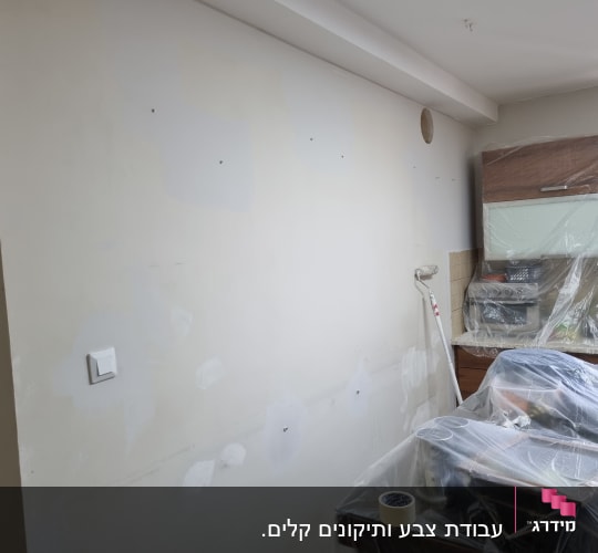 קיר עם תיקוני צבע, רולר ומוצרים מכוסים בניילון